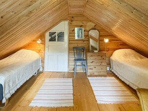 Un dormitorio acogedor en el ático con dos camas, una silla, un aparador y un espejo.