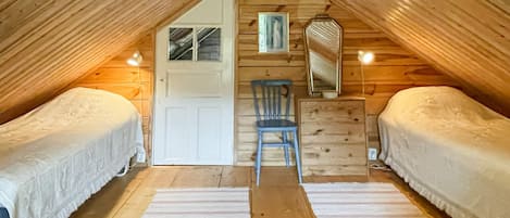 A small, cozy attic bedroom with two beds, a chair, a dresser, and a mirror.