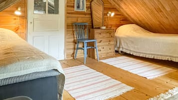 A cozy attic bedroom with two beds, a wooden chair, a small table, and a mirror on the wall.
