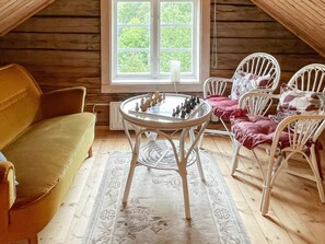 A cozy room with a wooden ceiling, a round table with chess pieces, a yellow sofa, and white chairs with red cushions. - 4 Person Holiday Home in Virserum (Virserum)