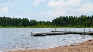 A sandy beach with a wooden dock extending into calm water, surrounded by dense forest. - 4 Person Holiday Home in Virserum (Virserum)