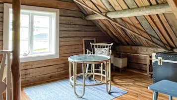 A wooden interior with a sloped ceiling, a round table with chairs, a window, and a small table with a chair.