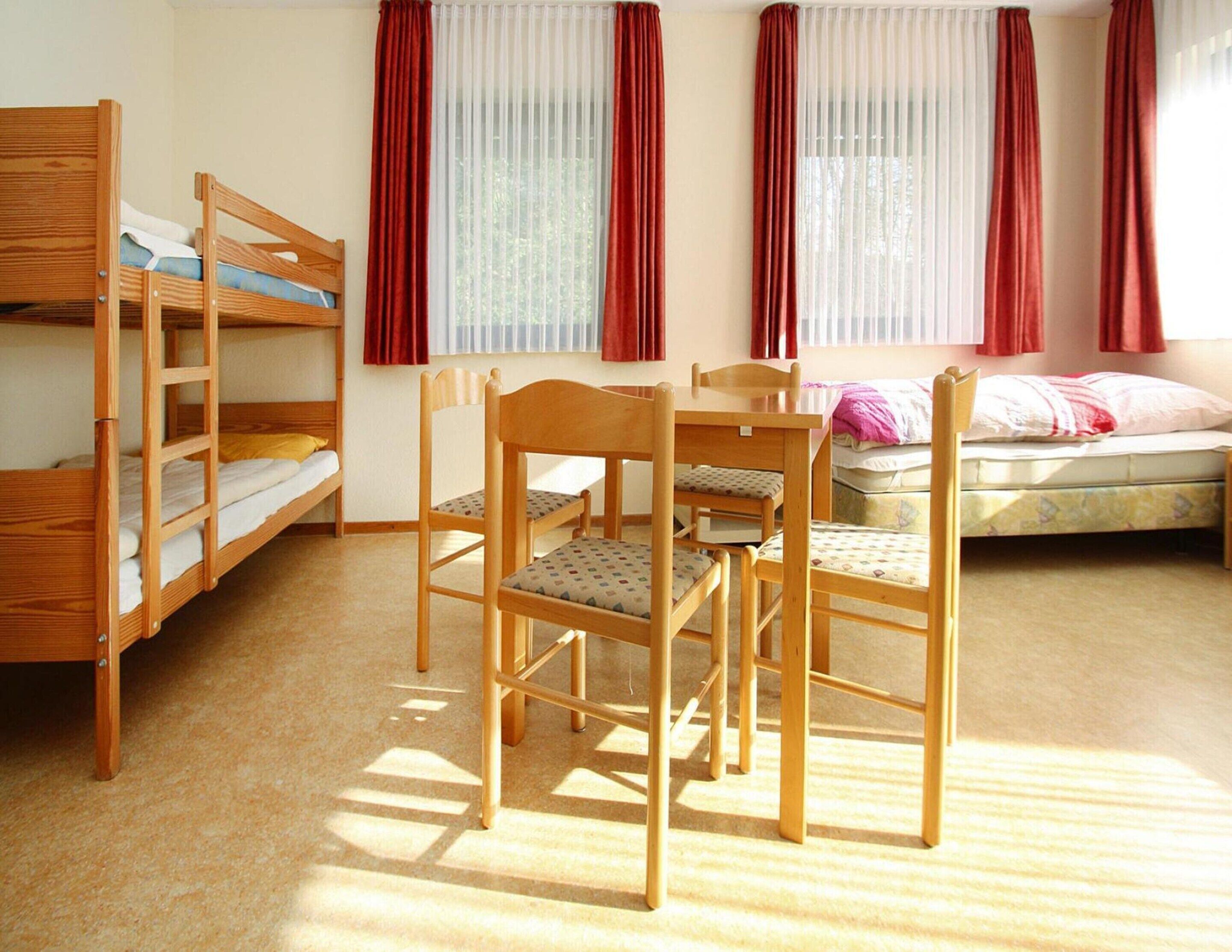 A dormitory room with bunk beds, a wooden table, and chairs.
