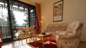 Ein Wohnzimmer mit einer Couch, Sesseln, einem Tisch und einem Balkon mit Glastür.