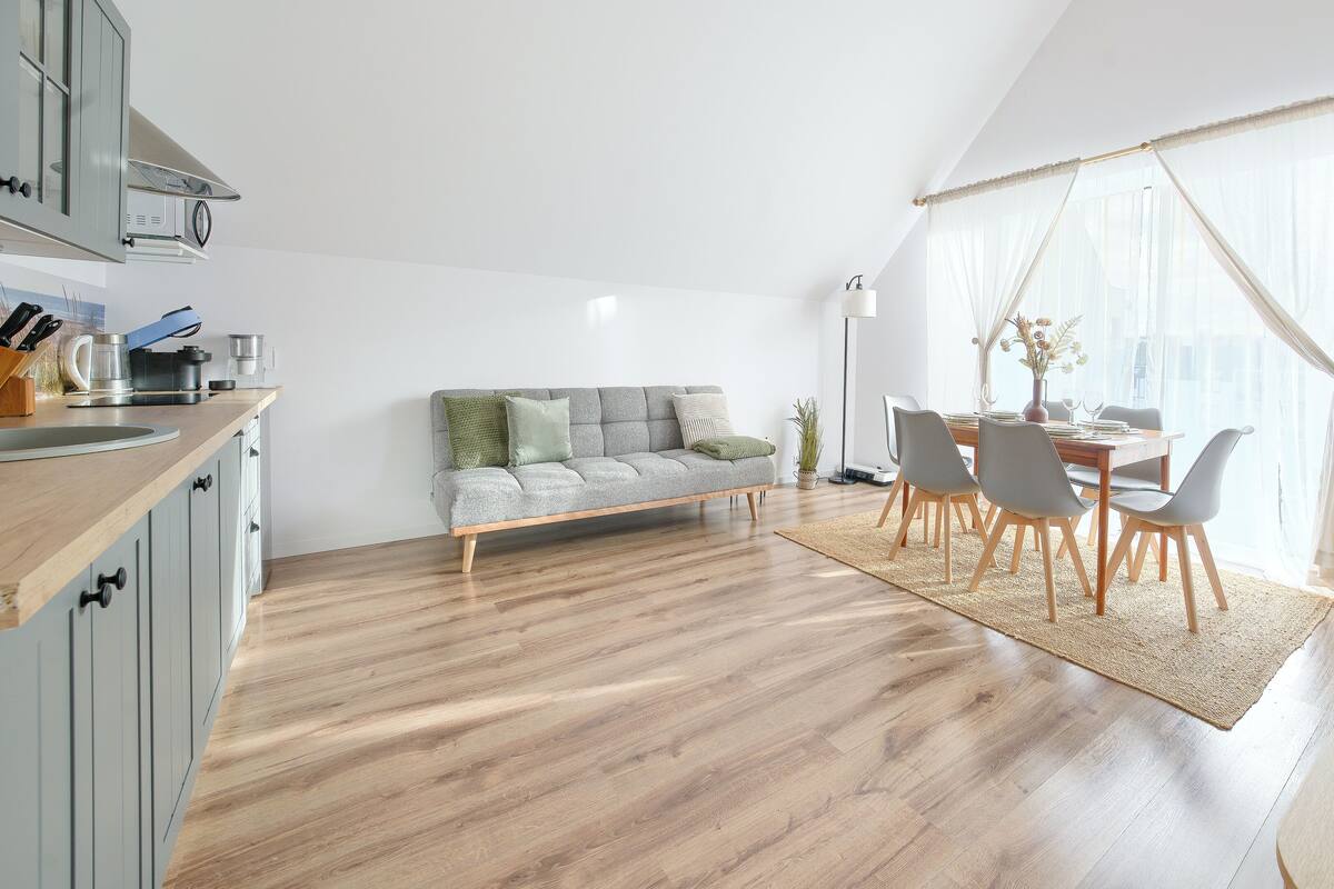 A modern kitchen with a wooden countertop, a grey sofa, and a dining area with a table and chairs.