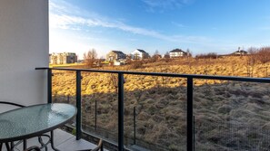 A balcony with a glass table and chairs, overlooking a hilly landscape with buildings in the distance. - Sun & Snow Słoneczne Apartamenty (Ustronie Morskie)
