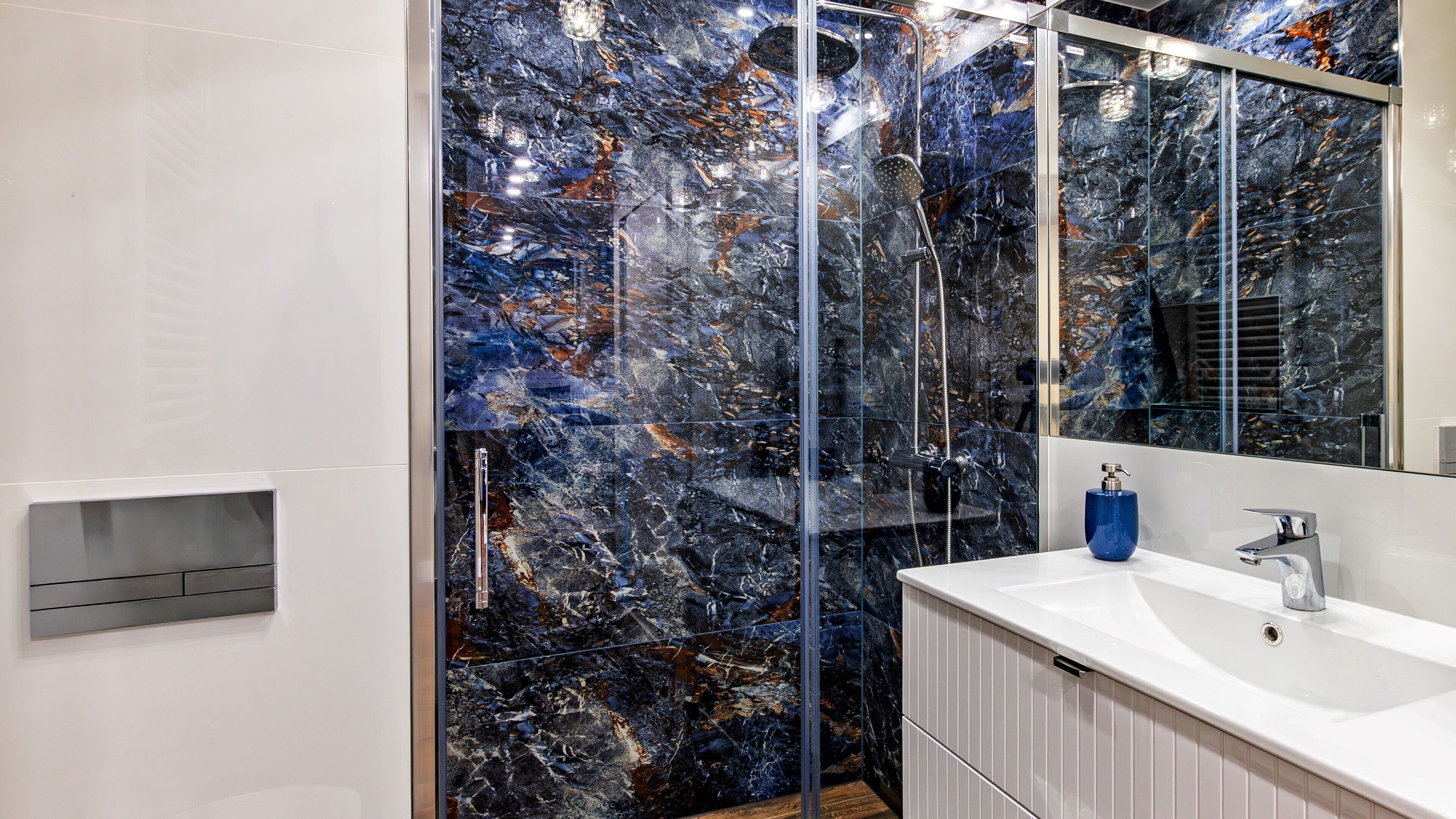 A modern bathroom with a glass-enclosed shower, a white sink, and a marble backsplash.