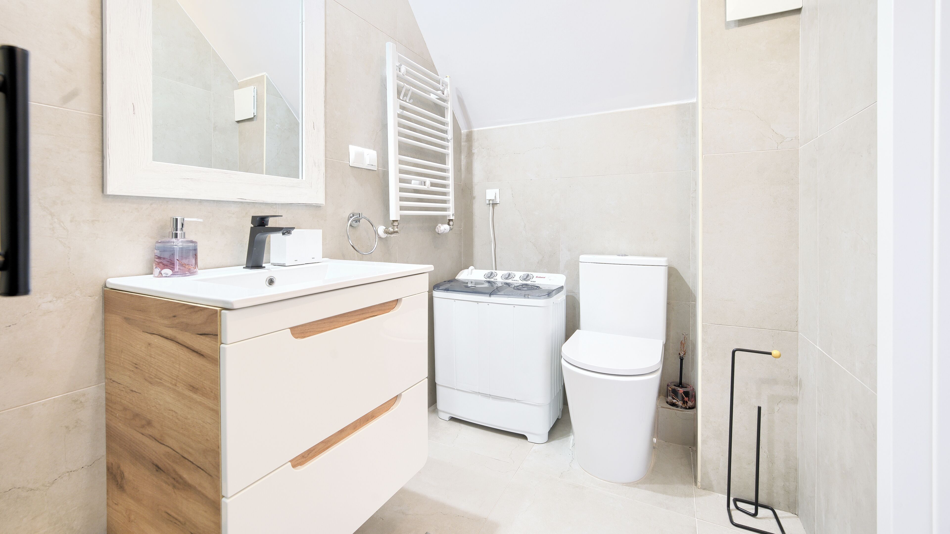 Ein modernes Badezimmer mit Waschbecken, Spiegel, Handtuchhalter, Toilette und Waschmaschine.