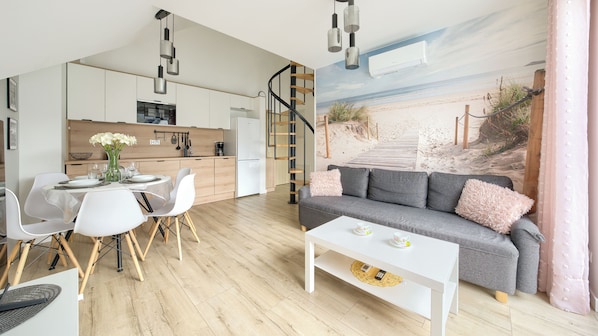 A modern living space with a dining area, a sofa, and a kitchen.