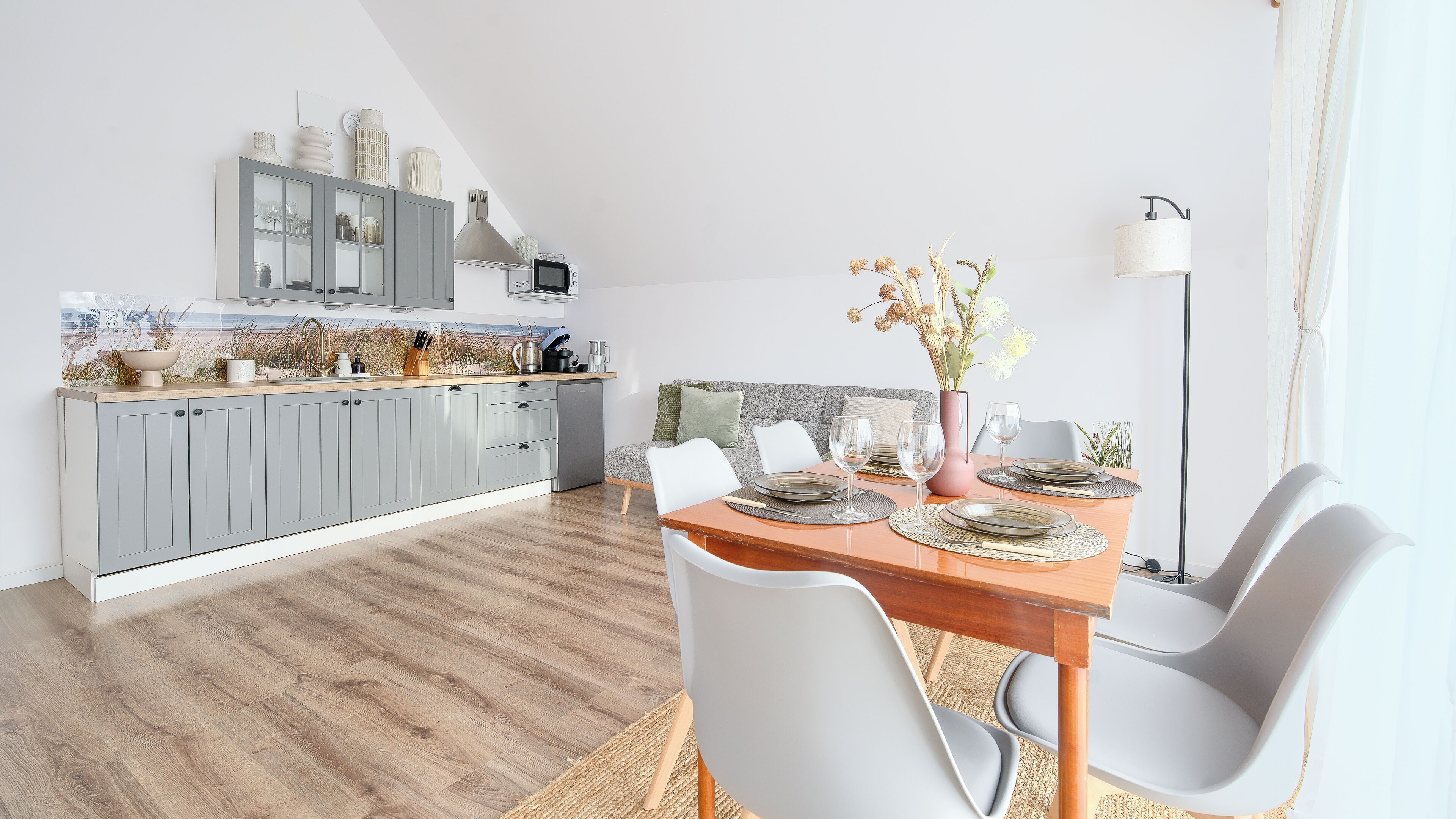 A modern kitchen with grey cabinets, a wooden countertop, and a dining area with a wooden table and white chairs.