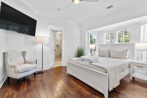 Ein Schlafzimmer mit einem großen Bett, einem Sessel, einem Nachttisch, einer Stehlampe und einem an der Wand befestigten Fernseher.
