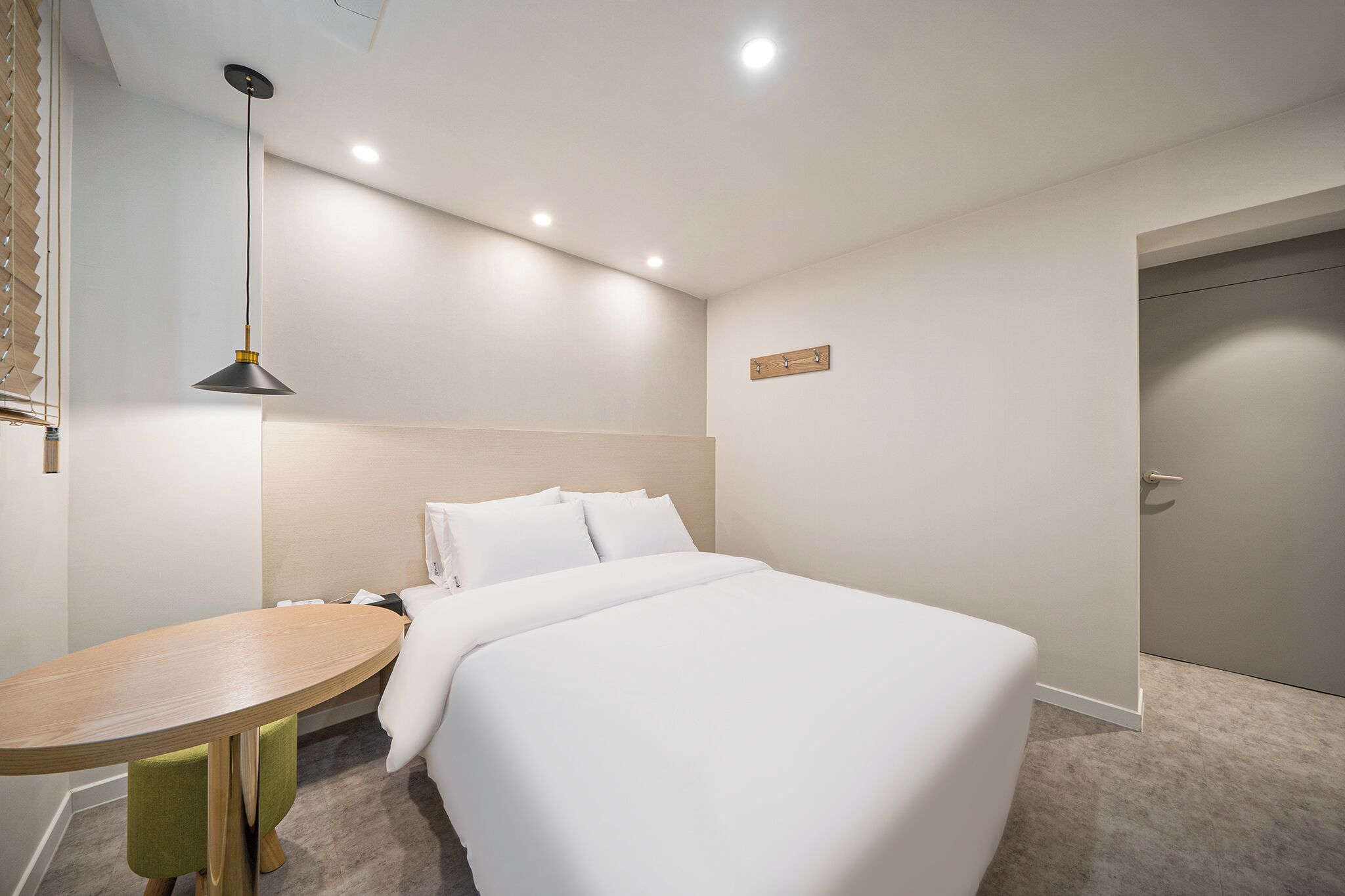 Habitació d'hotel amb un llit, una taula rodona petita, una làmpada penjant i una porta.