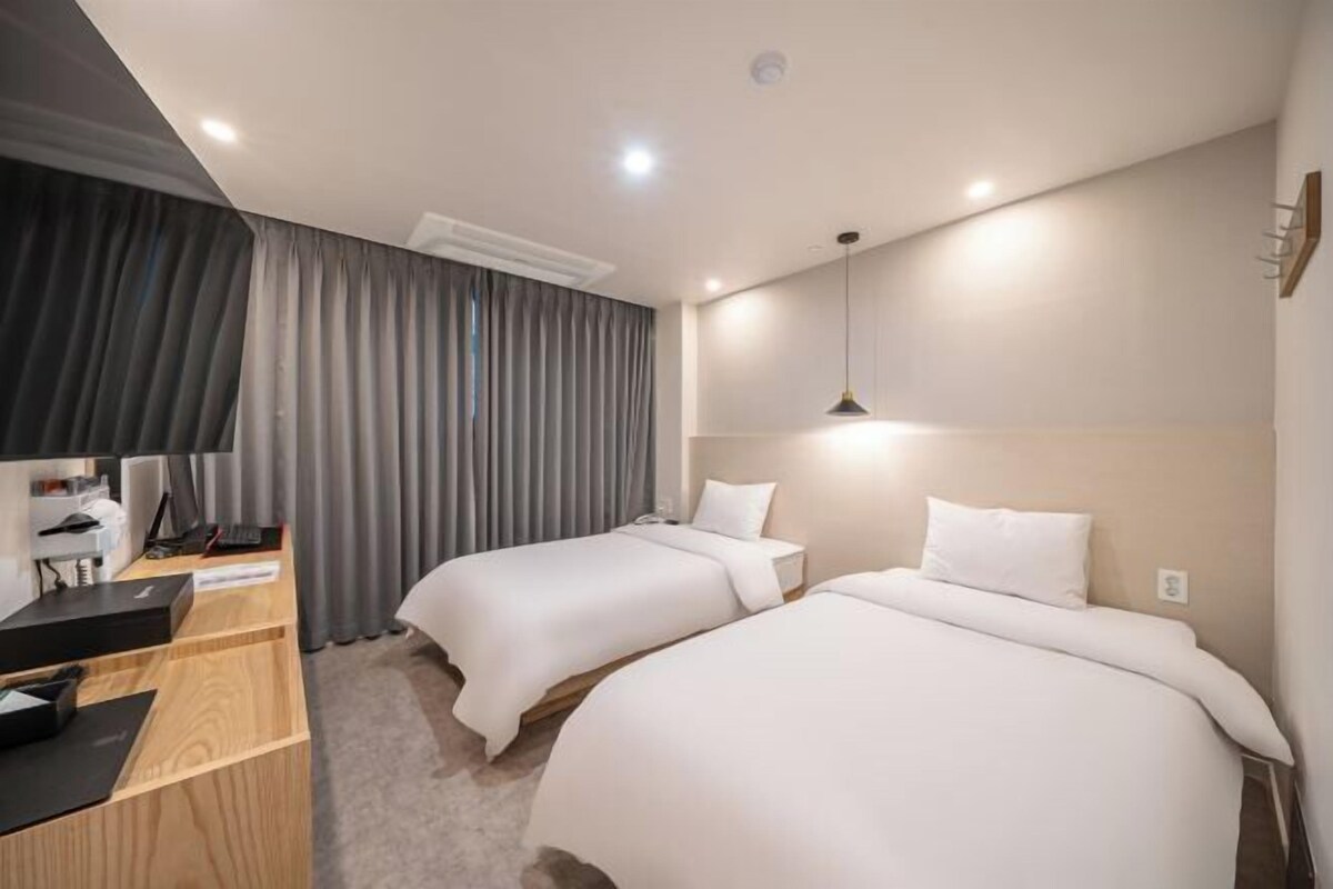 A hotel room with two beds, a desk with a computer, and a large window with curtains.