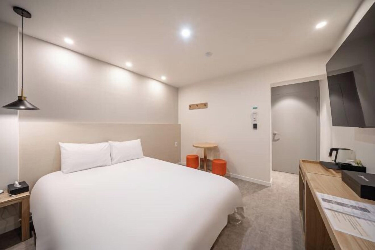 A hotel room with a large bed, a desk with a chair, a small round table, and a lamp.