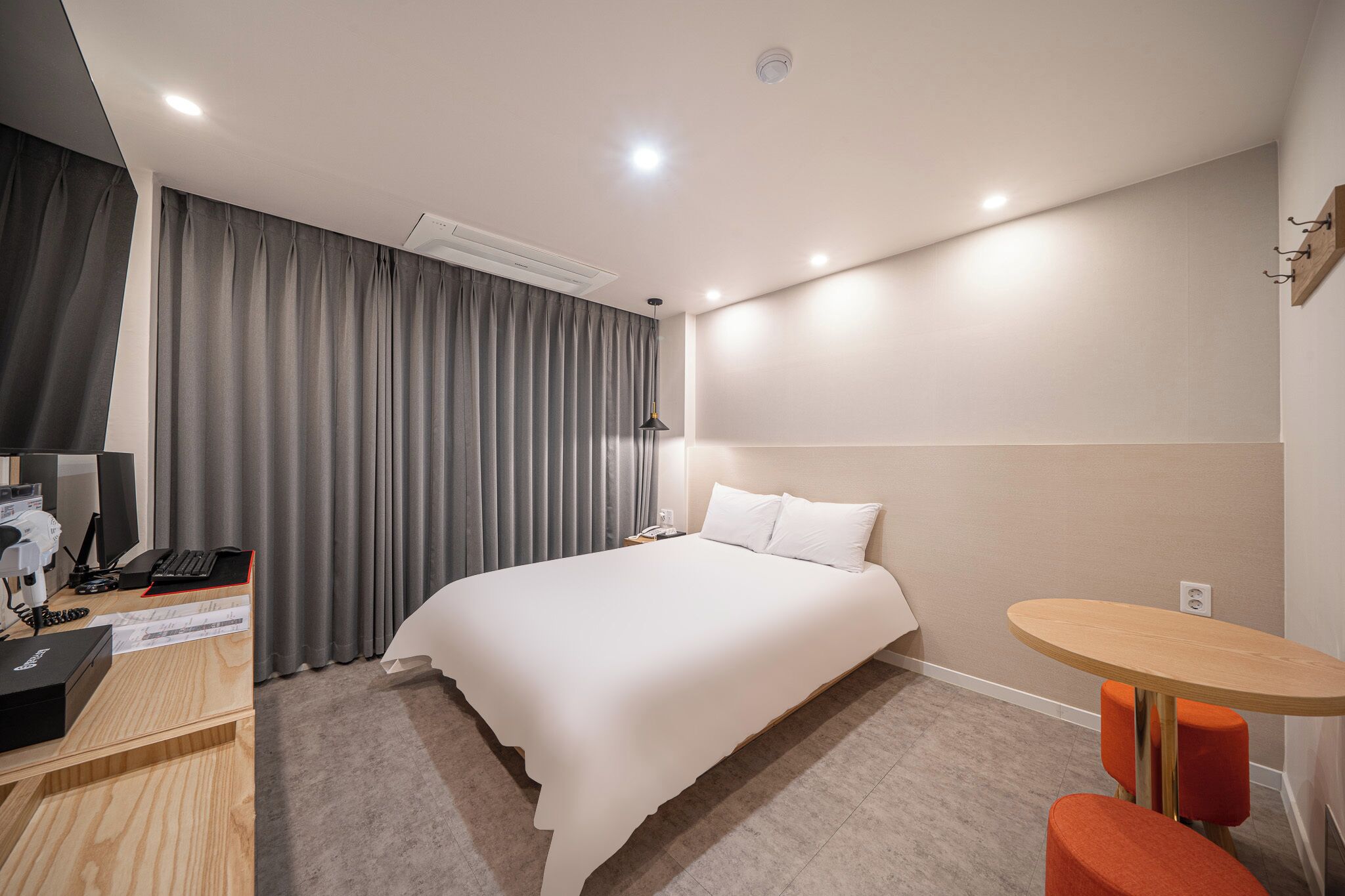 A modern hotel room with a large bed, a desk with a computer, a small round table, and a chair.