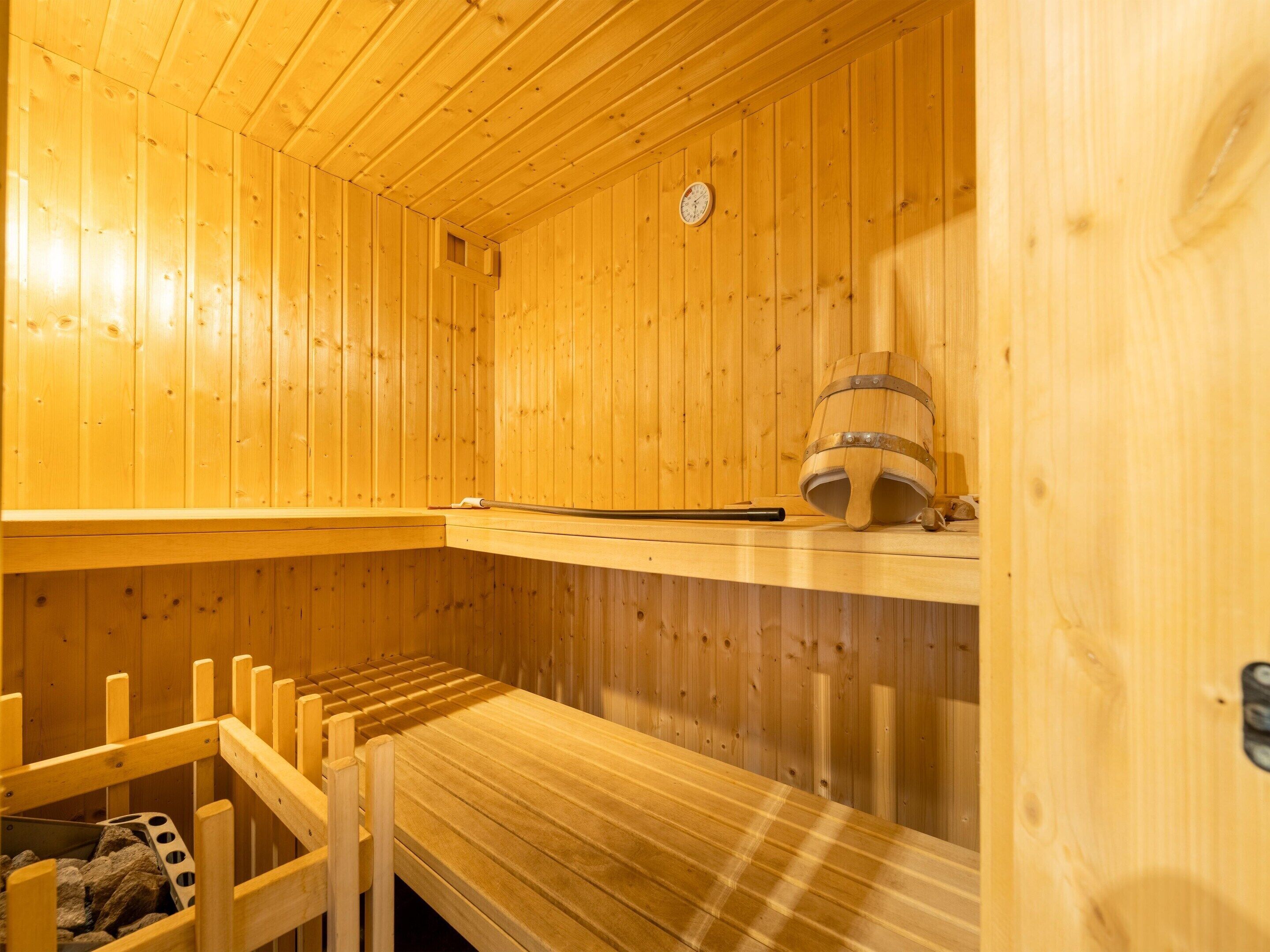 Una sauna de madera con bancos, un cubo de madera y un reloj en la pared.
