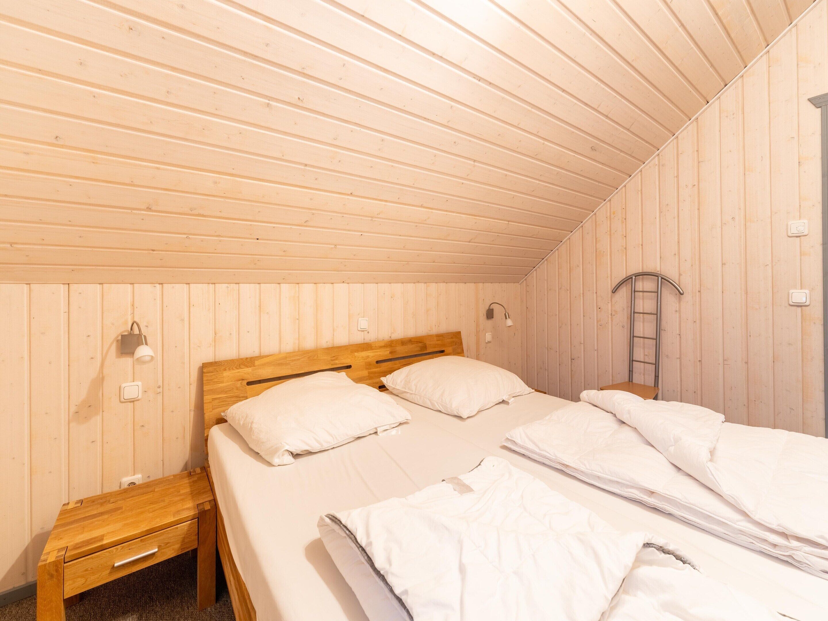 A wooden-paneled room with two beds, a nightstand, and a ladder.