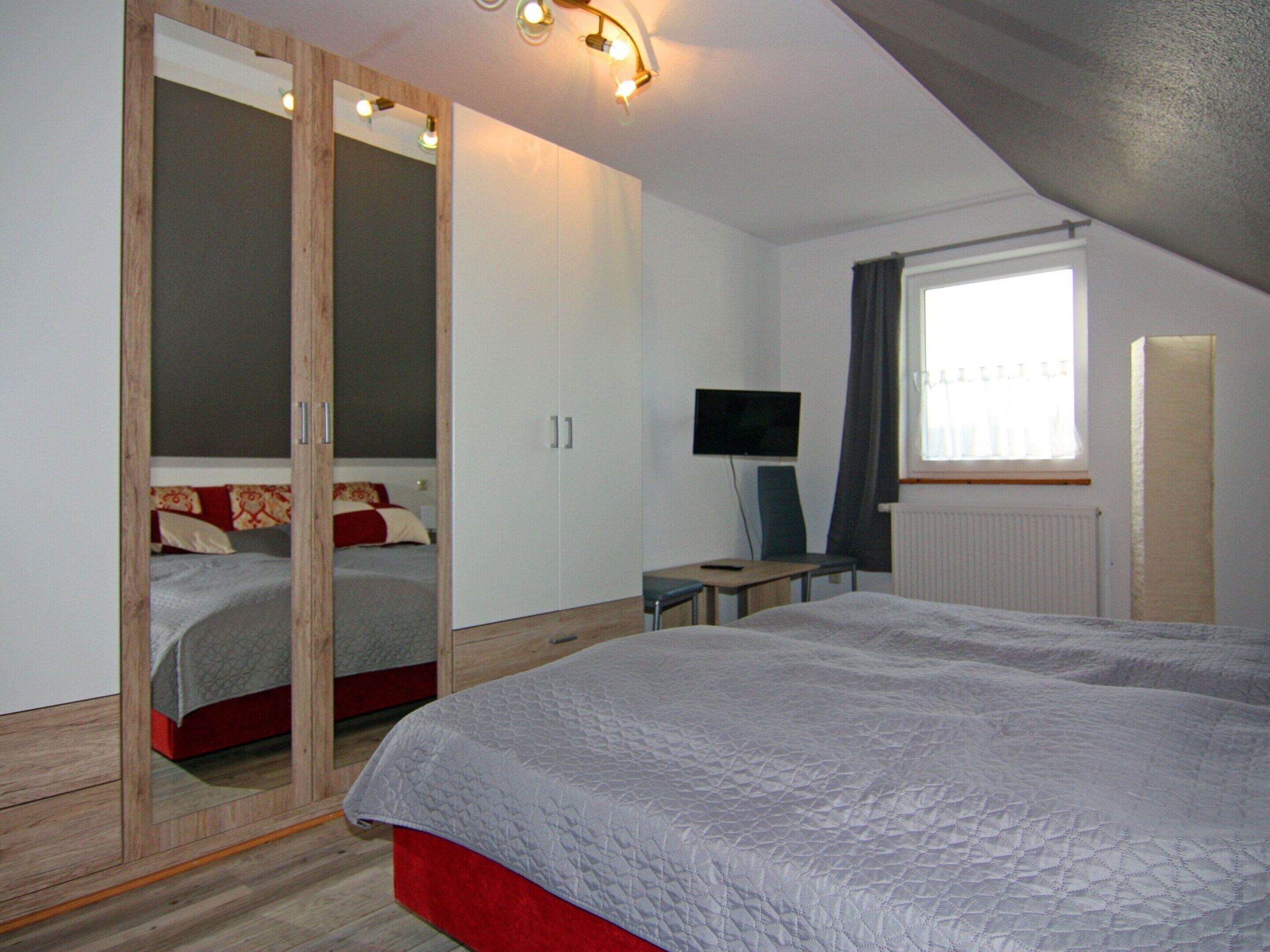 A bedroom with a bed, a desk, a TV, and a wardrobe.