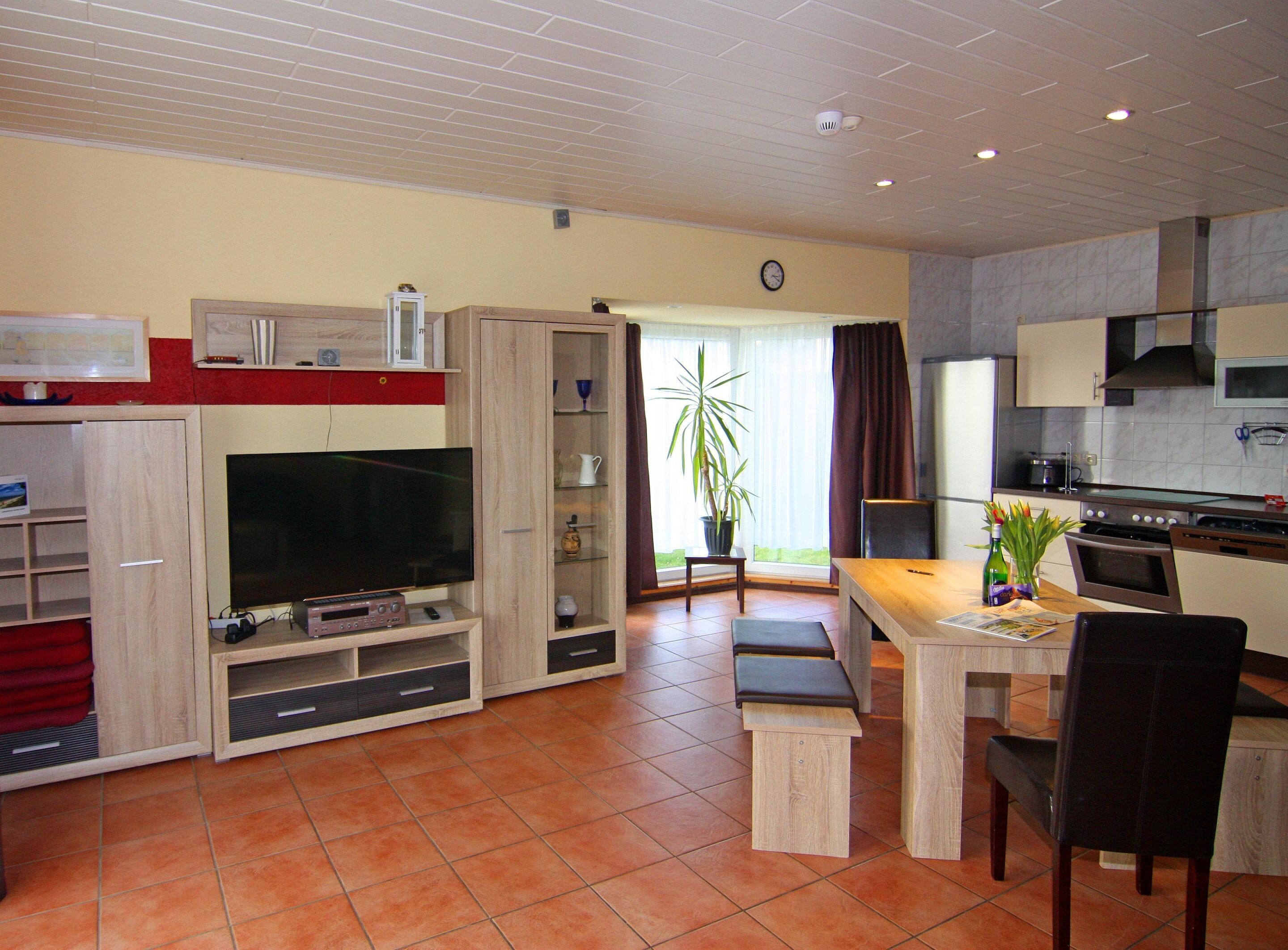 A living room with a TV, entertainment unit, and a dining area with a table and chairs.