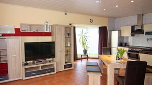 A modern living room with a flat-screen TV, wooden cabinets, a dining area with a table and chairs, and a kitchen with a stove and microwave. - Doppelhaushalfte in Bansin (Heringsdorf)