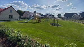 A playground with slides and swings, surrounded by stone buildings with red roofs. - Well-kept and Cozy Polder House (Koksijde)