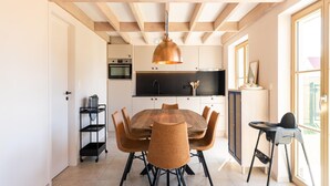 A modern kitchen with wooden beams, a dining table with chairs, and a large window. - Well-kept and Cozy Polder House (Koksijde)