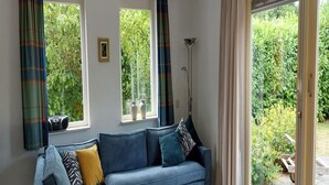 A living room with a blue sofa, a small white table, and a view of a garden through large windows. - Nice Holiday Home Near Beach (Wemeldinge)
