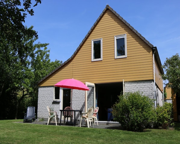 A two-story house with a gabled roof, a front porch with a table and chairs, and a pink umbrella. - Nice Holiday Home Near Beach (Wemeldinge)
