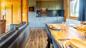 Una cucina accogliente in stile baita, con pareti in legno, un forno a microonde integrato e un'area pranzo con un tavolo di legno apparecchiato per due.