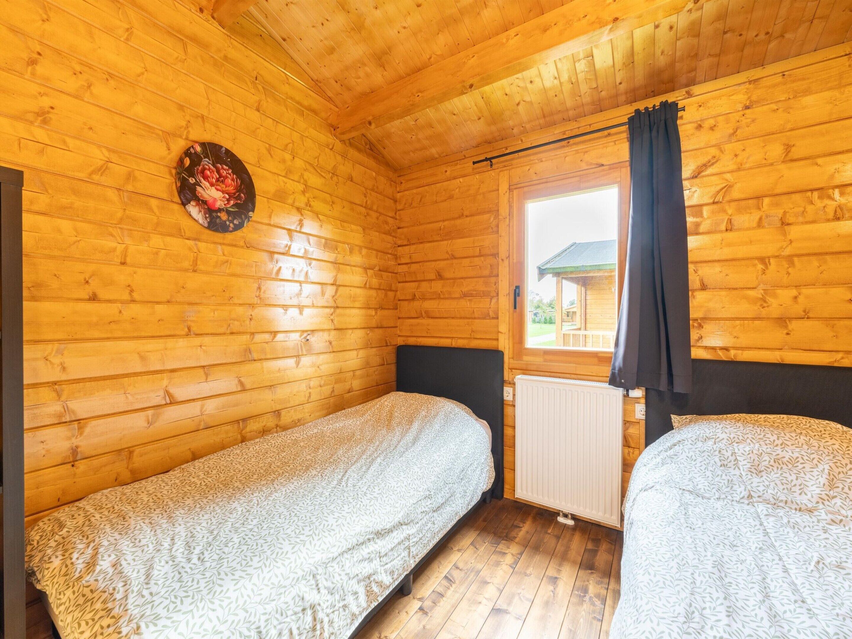 Habitació d'una cabana de fusta amb dos llits, una finestra amb cortines i un radiador.