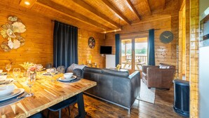 Un accogliente interno di una baita in legno, con zona pranzo, divano e vista su una terrazza esterna attraverso una porta vetrata.