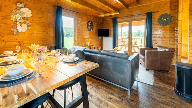 Interno di una baita in legno con zona pranzo, divano e vista sull'esterno.