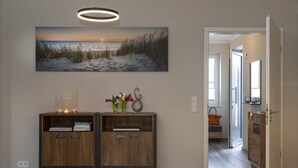 Ein Flur mit einem Holzkonsolentisch, einem Gemälde einer Strandansicht und einer Tür zu einem weiteren Zimmer.