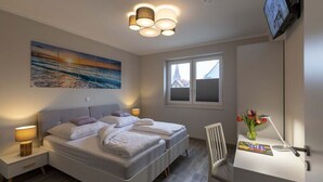 Ein Schlafzimmer mit zwei Betten, einem Schreibtisch mit Stuhl, einem Fernseher und einem Fenster mit Blick auf Gebäude.