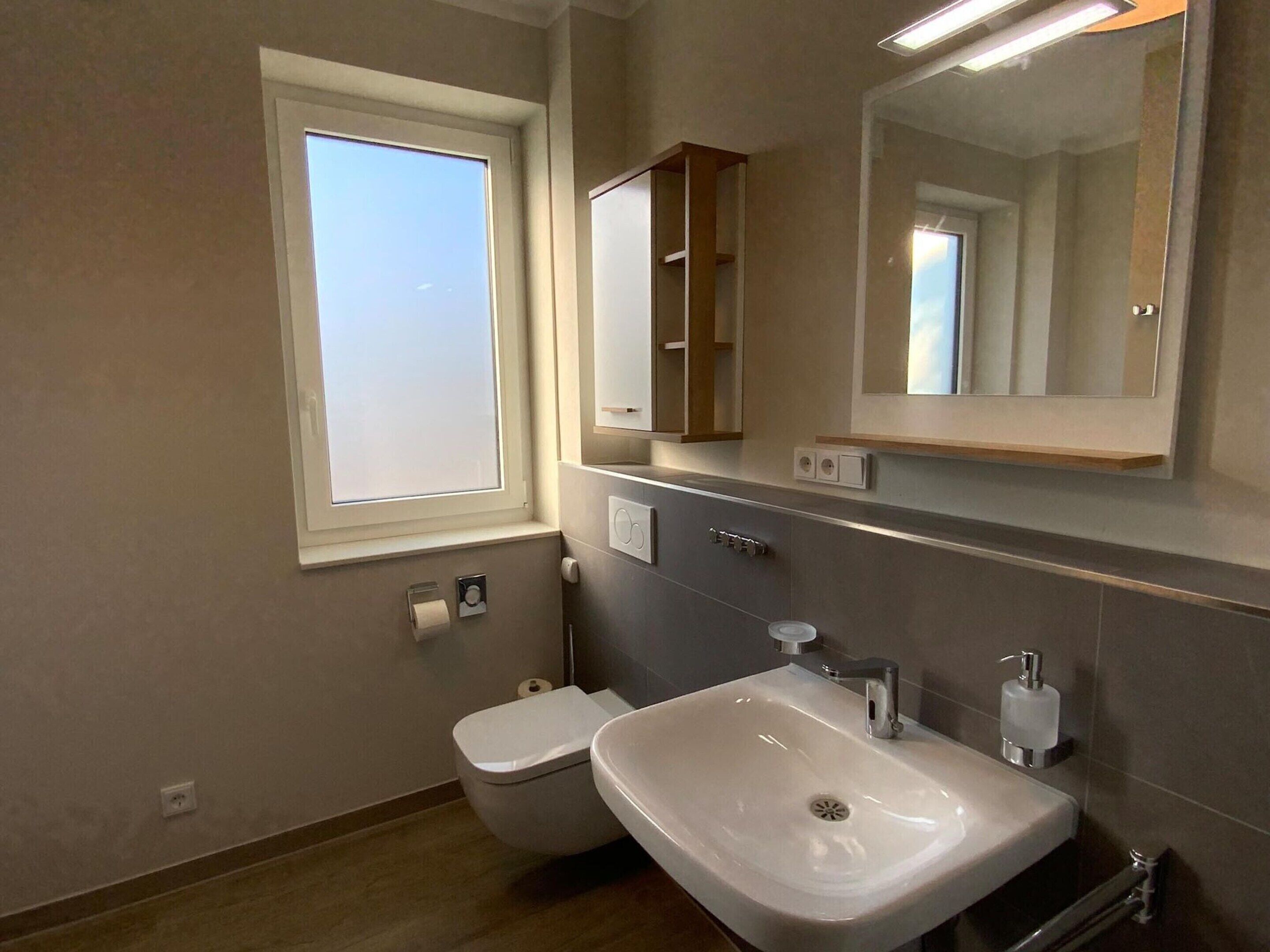 A modern bathroom with a toilet, sink, and mirror.