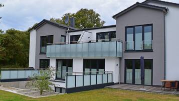 Une maison moderne à deux étages, dotée d’un balcon, de grandes fenêtres et d’un petit jardin.