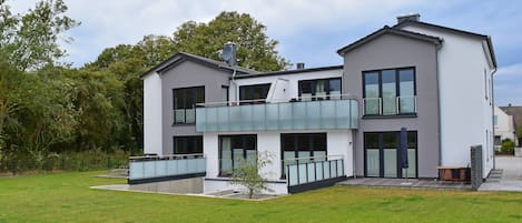 A modern two-story house with a balcony, large windows, and a well-maintained lawn.