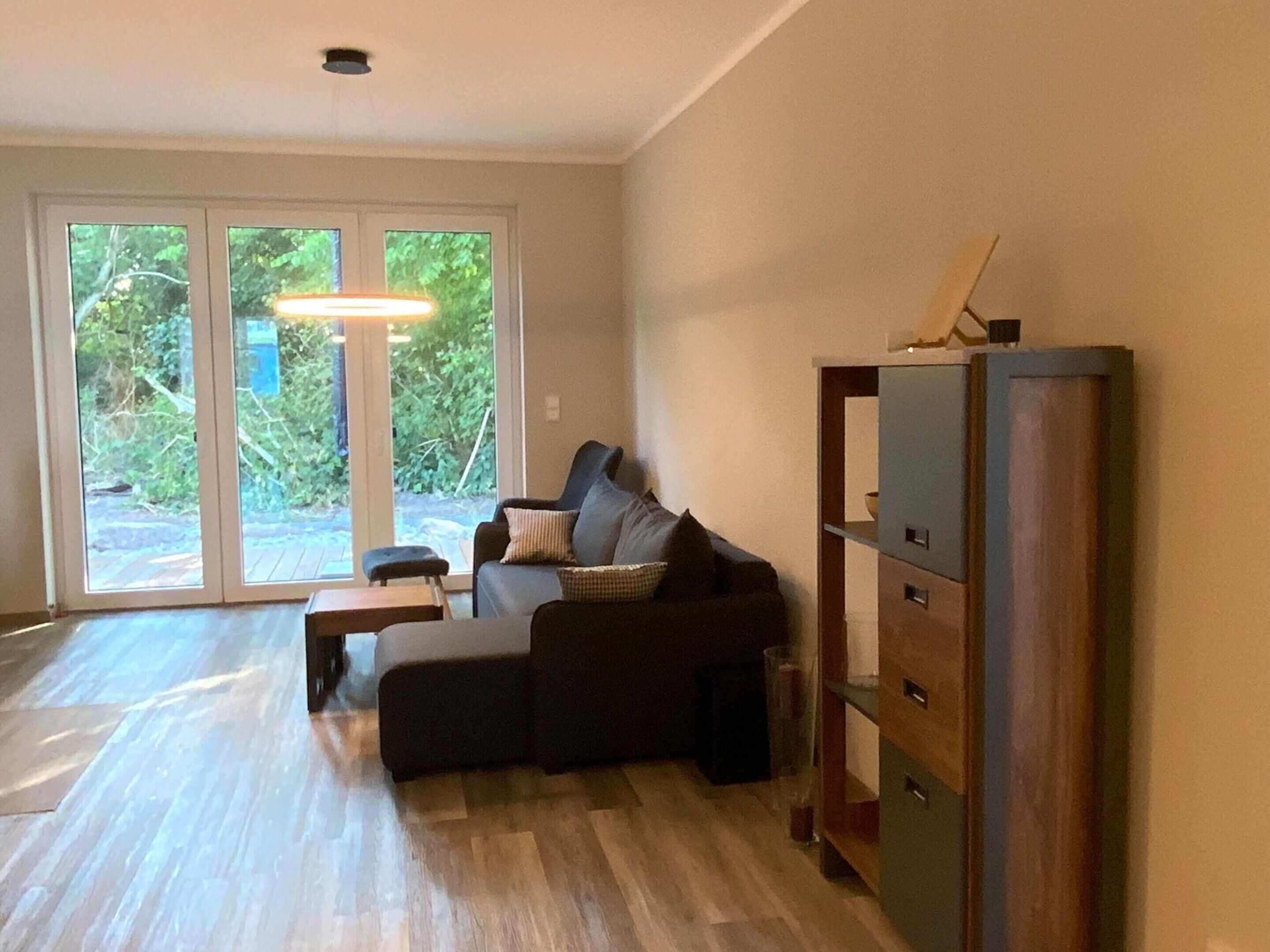 Un salon comprenant un canapé, une table basse et un meuble. Une porte-fenêtre coulissante donne accès à un espace extérieur.