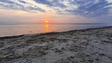 Une plage au coucher du soleil, avec un ciel dégagé et une mer calme.