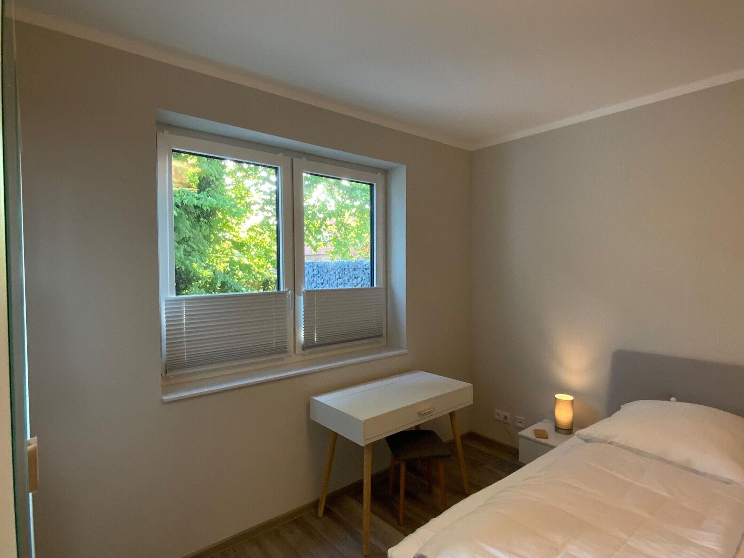 A bedroom with a bed, a desk, and a window with blinds.