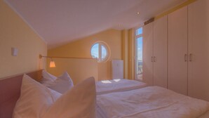 A bedroom with two beds, a round window, and a wardrobe. - Apartment in Granzow Near the Lake (Mirow)