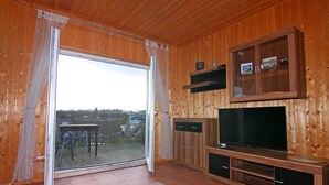 Una habitación con paneles de madera, una puerta corrediza de vidrio que da a una terraza exterior, un televisor y estanterías empotradas.