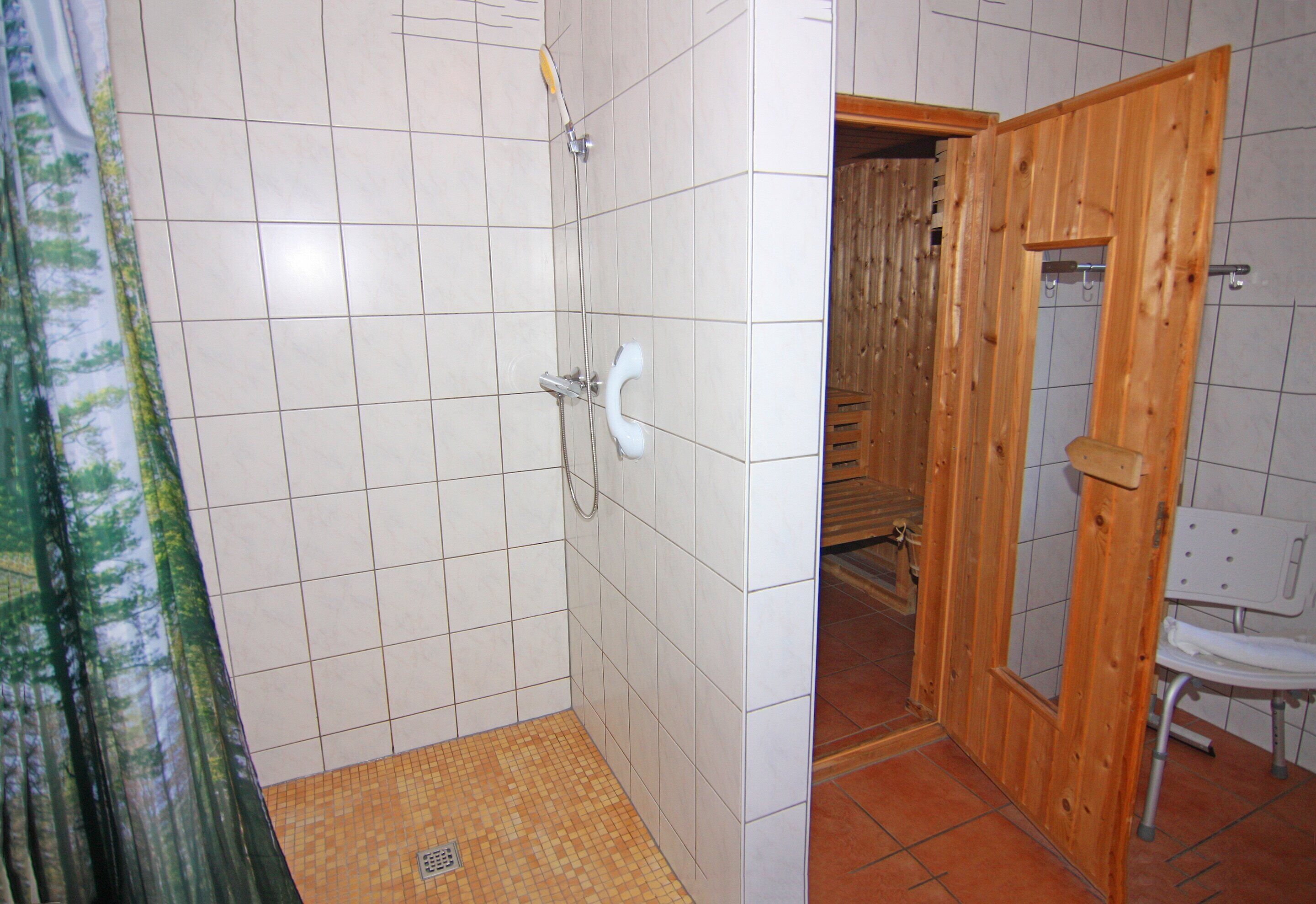 A bathroom with white tiled walls, a wooden door, and a shower area.