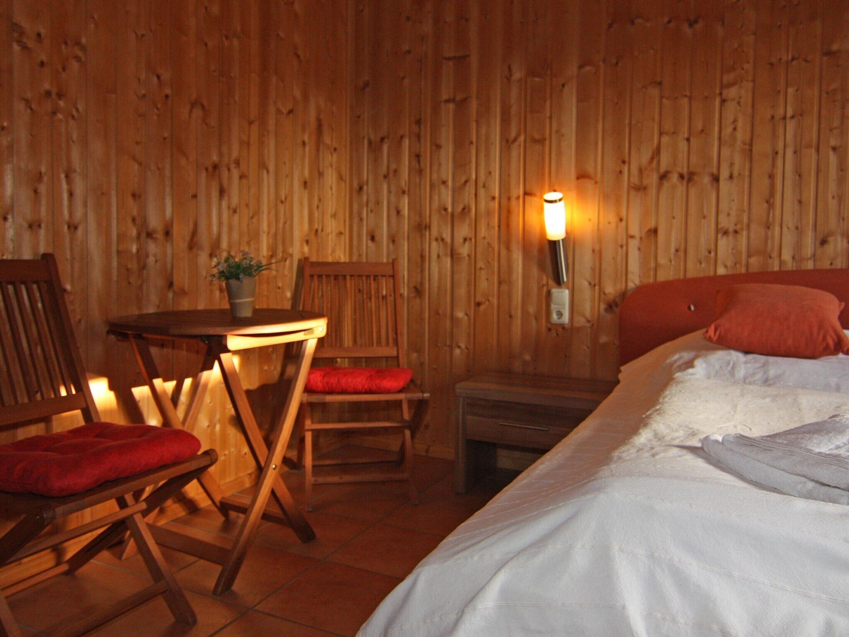 A wooden room with a bed, a table, and two chairs.