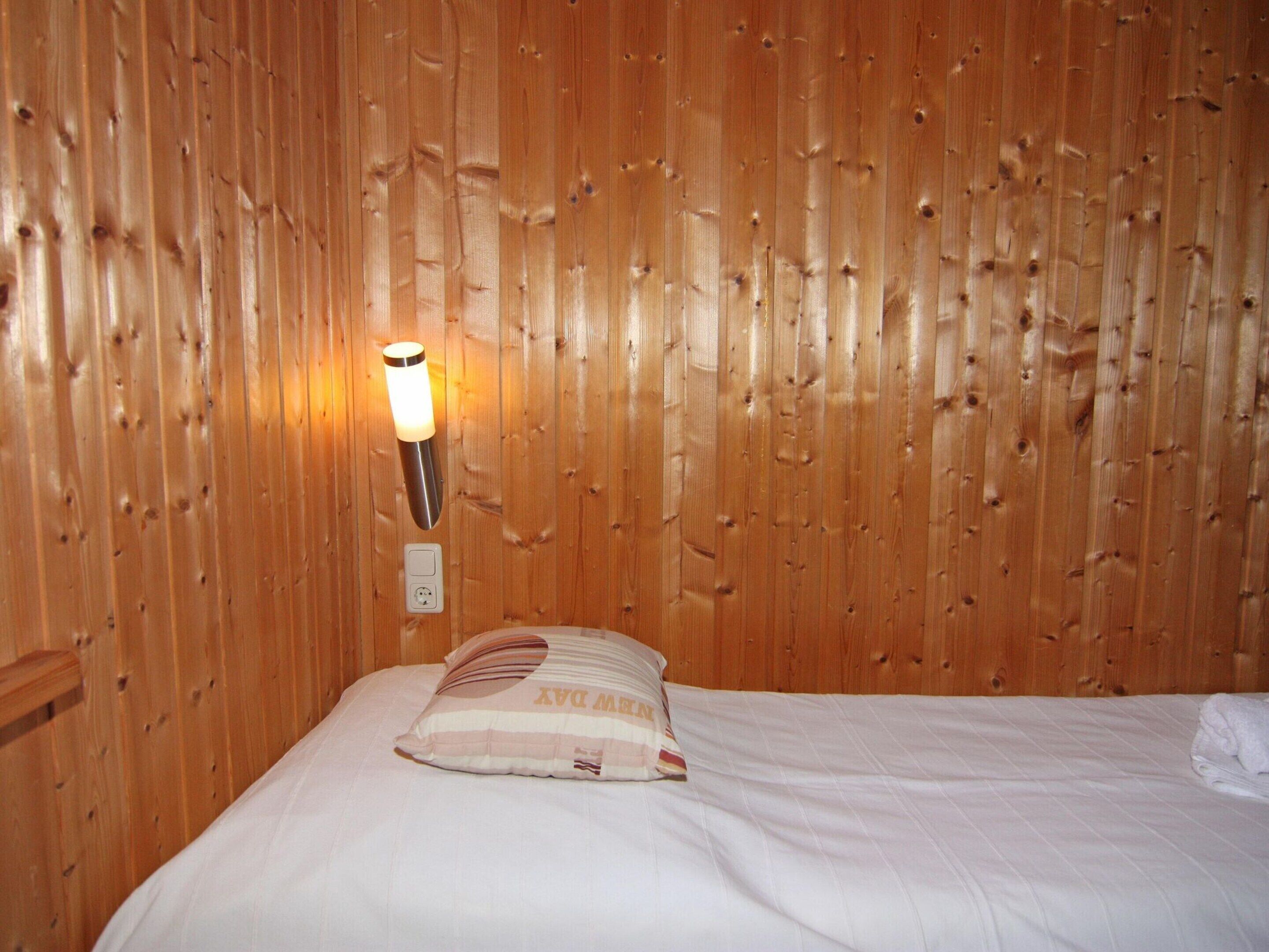Una habitación con paneles de madera, una cama, una lámpara fijada a la pared y un enchufe.