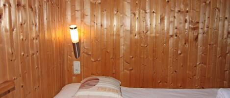 Una habitación con paneles de madera, una cama, una lámpara fijada a la pared y un enchufe.