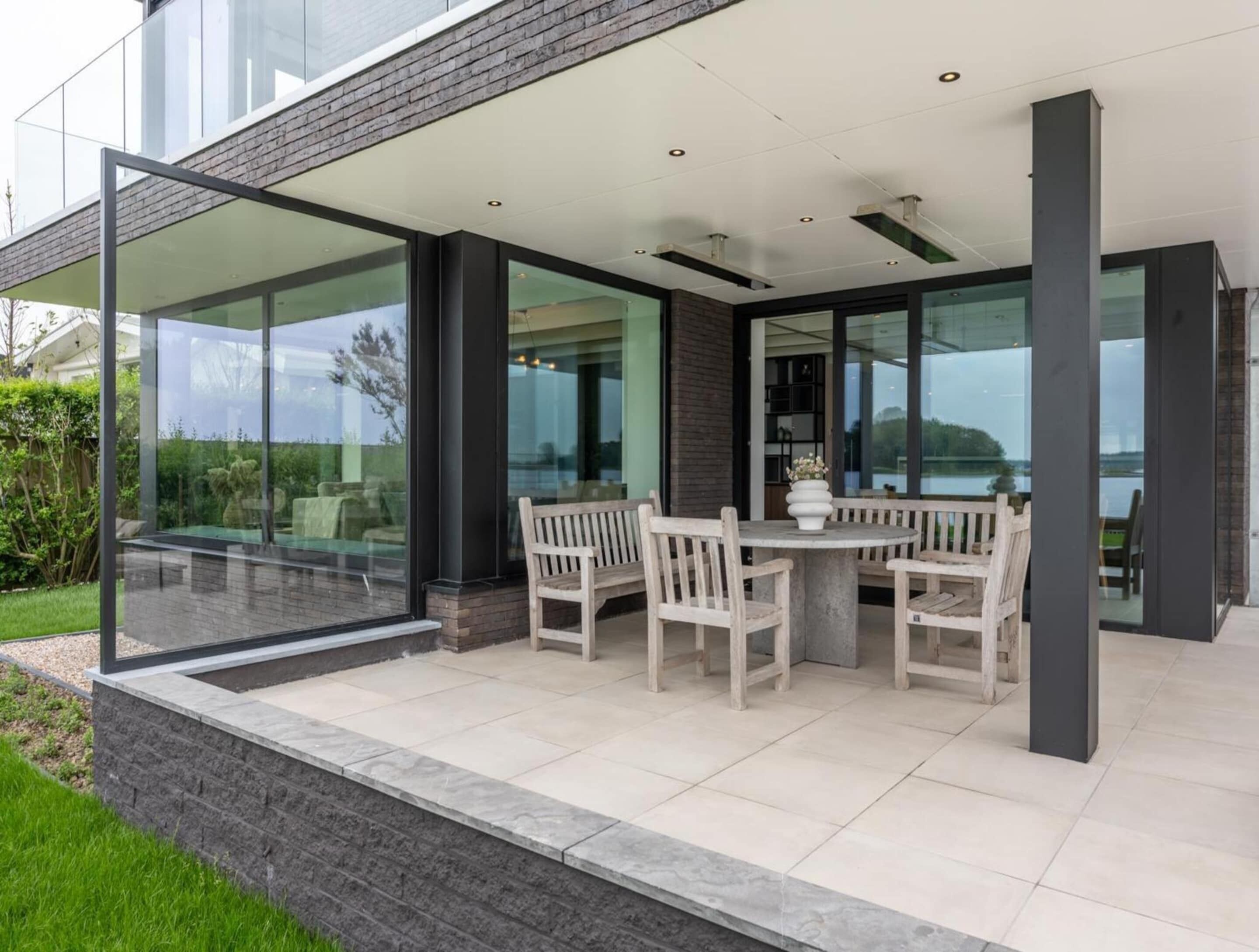 A modern outdoor patio with a glass enclosure, a round table, and wooden chairs.