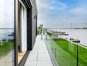 Ein modernes Gebäude mit einem Glasbalkon und Blick auf ein Gewässer sowie eine Anlegestelle.
