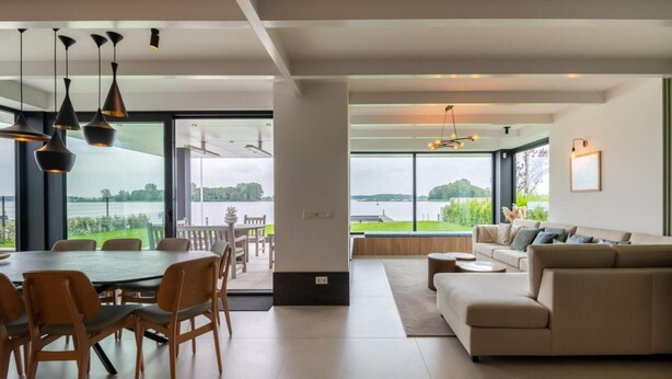 A spacious living area with a large dining table, a sofa, and a view of a lake. - Attractive Villa With Jetty (Kamperland)