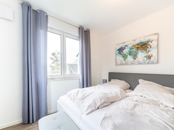 A bedroom with a bed, grey curtains, a world map artwork, and a window with a view of a house.